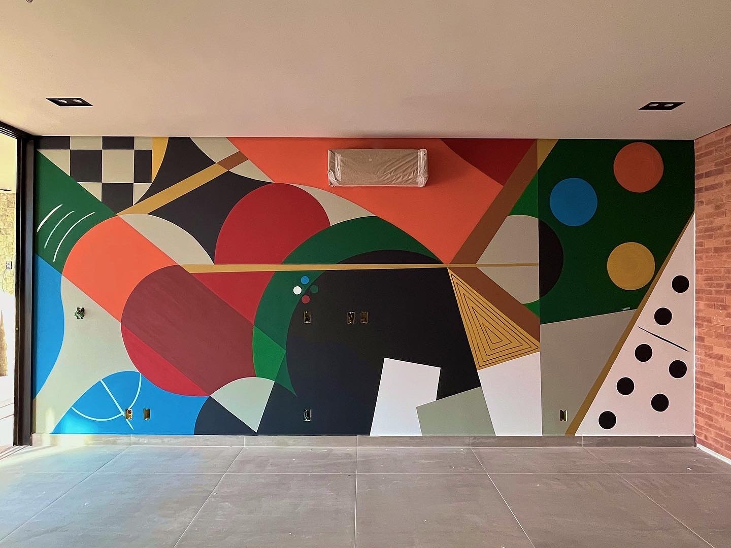 Mural geométrico colorido integrado à arquitetura de um ambiente interno.